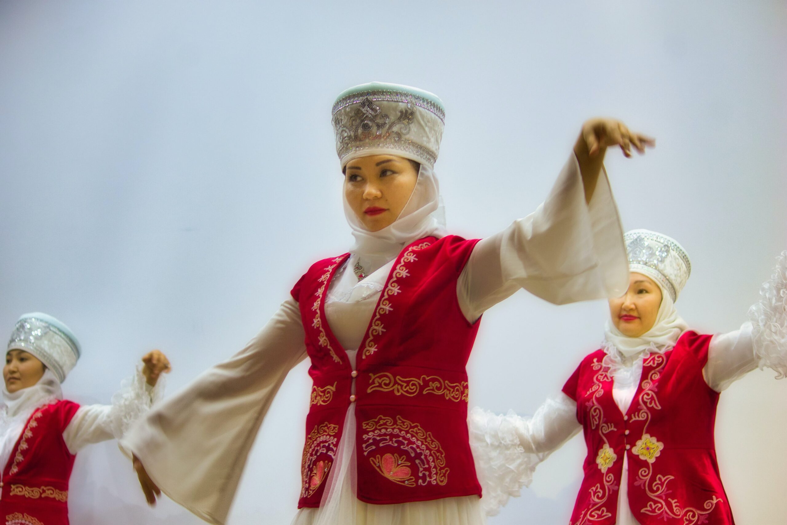 A Kyrgyz woman dressed in traditional garb dances with an ensamble